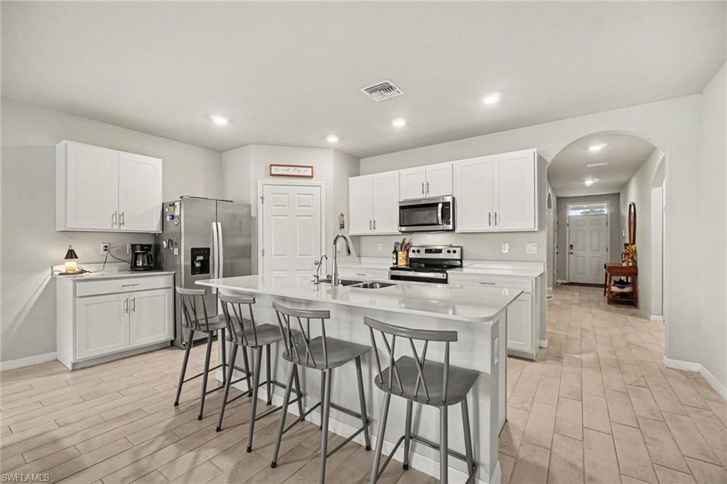Kitchen featuring white cabinetry, stainless steel appliances, a center island with sink, light-toned wood-finish flooring, and recessed lighting