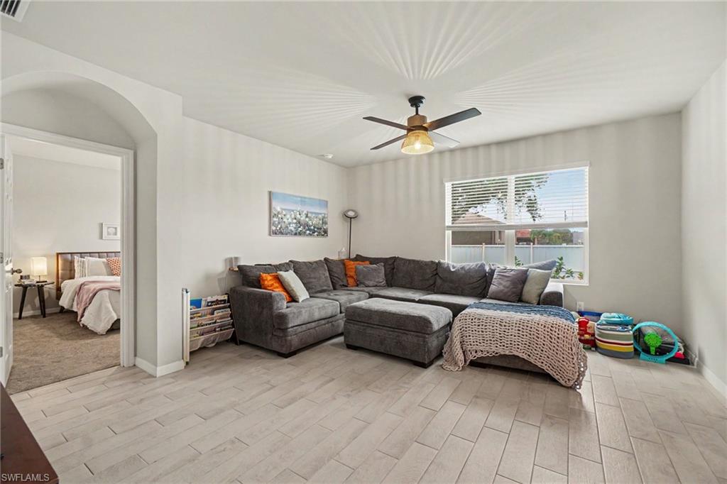 Open living area featuring light-toned wood-finish flooring, a contemporary ceiling fan with integrated lighting, and a large window with blinds