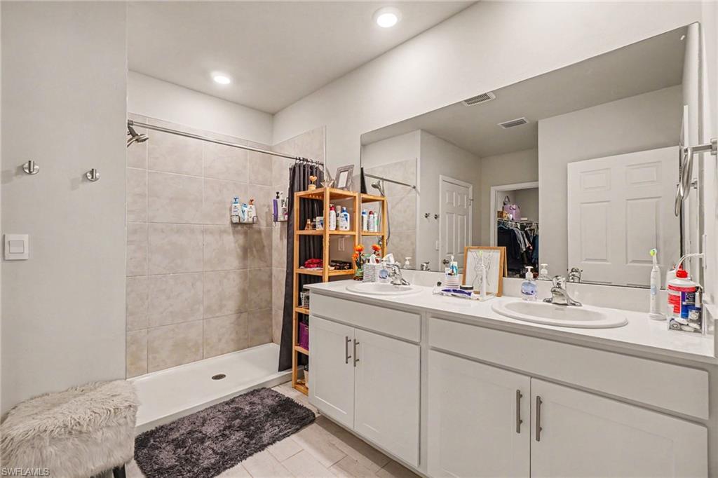 Bathroom featuring a double vanity with integrated sinks, a large wall-mounted mirror, and a shower with light-toned wall tiling