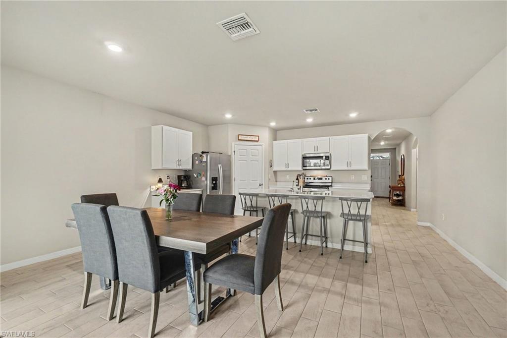 Open-concept living space featuring wood-finish flooring, recessed lighting, and a white kitchen with stainless steel appliances