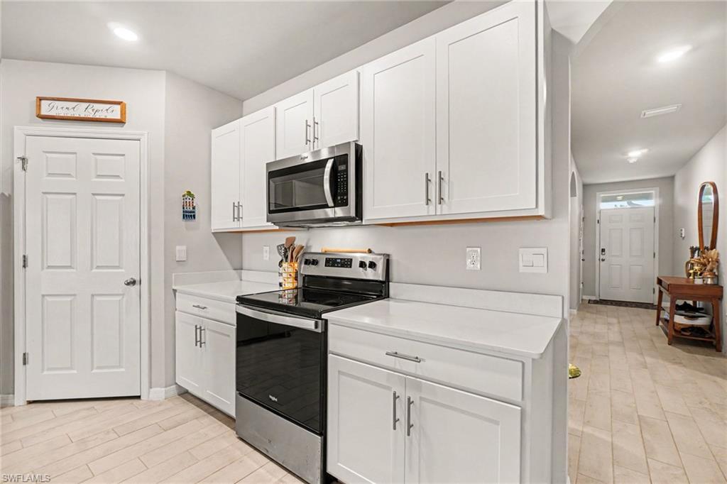 Kitchen featuring white shaker-style cabinetry, stainless steel appliances, light-toned countertops, and wood-finish flooring