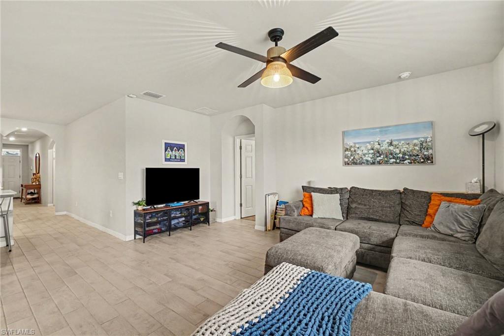 Open living area featuring light-toned tile flooring, a ceiling fan with integrated lighting, and arched doorways