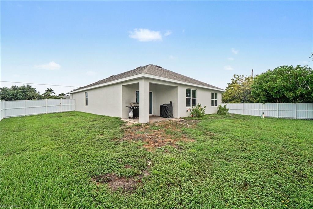 Expansive rear yard featuring a white privacy fence, green lawn space, and a covered patio area with a concrete slab