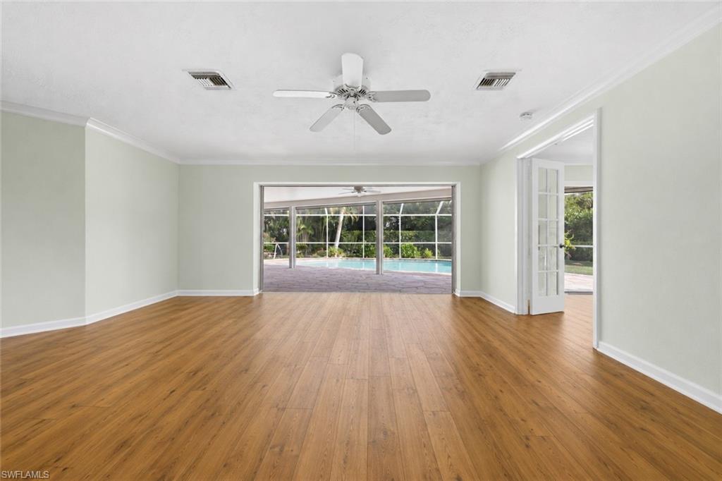 Bright, open living area with warm wood flooring, abundant natural light, and views toward the screened pool and lanai.