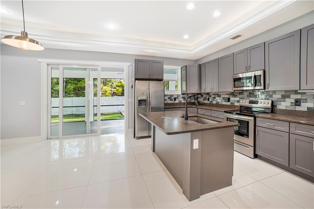 Kitchen featuring a kitchen island with sink, stainless steel appliances, backsplash, pendant lighting, and gray cabinets