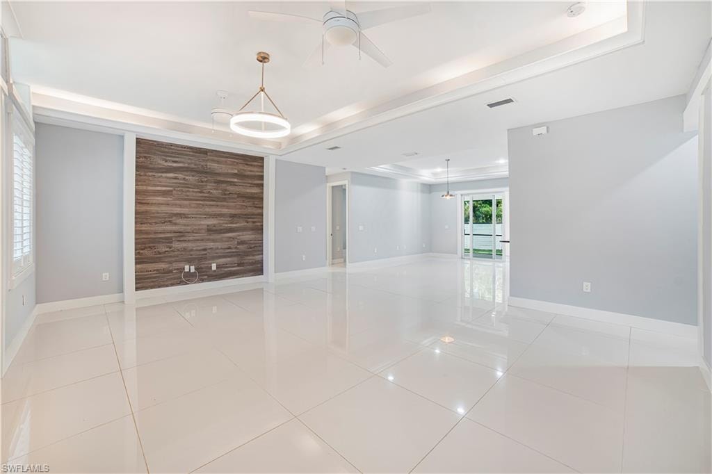 Spare room featuring ceiling fan, a tray ceiling, and light tile patterned floors