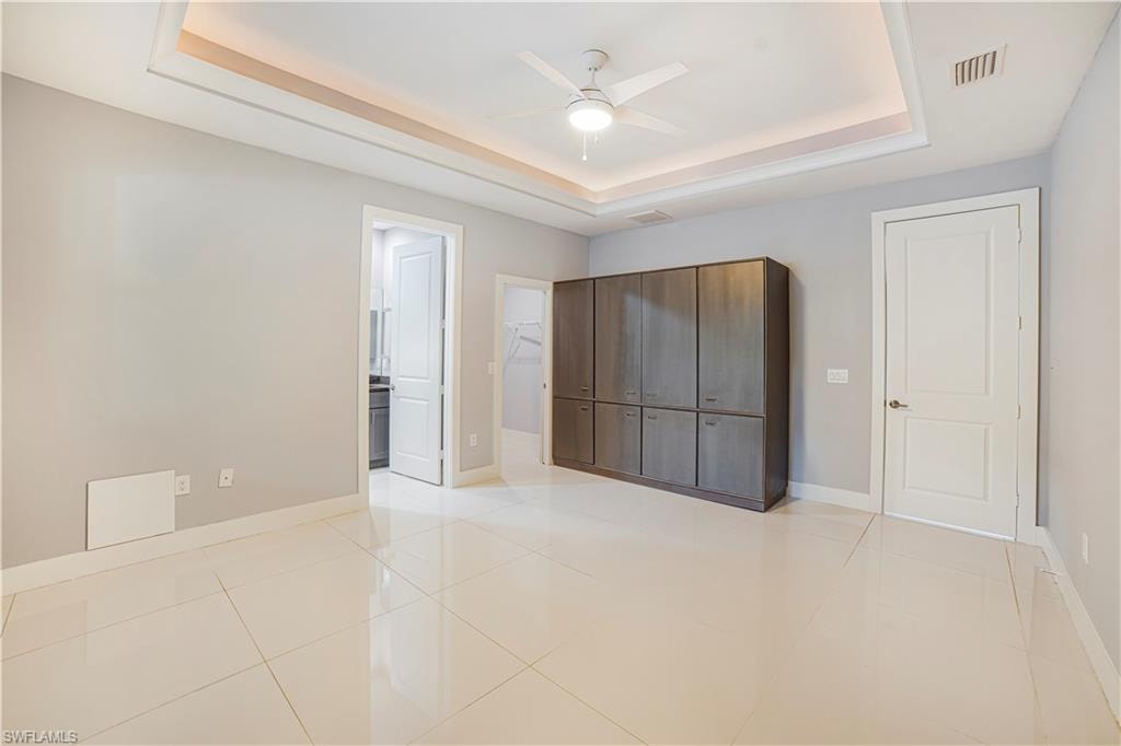 Unfurnished bedroom featuring ensuite bath, ceiling fan, light tile patterned floors, and a raised ceiling