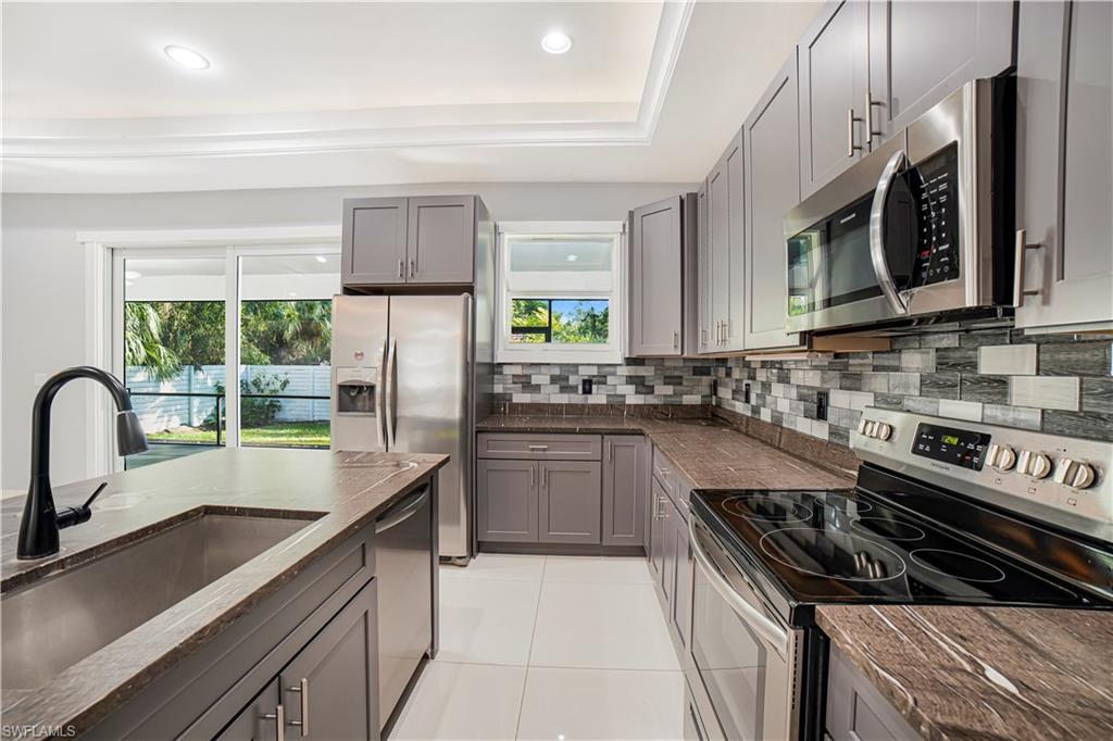 Kitchen with a raised ceiling, backsplash, sink, gray cabinetry, and stainless steel appliances
