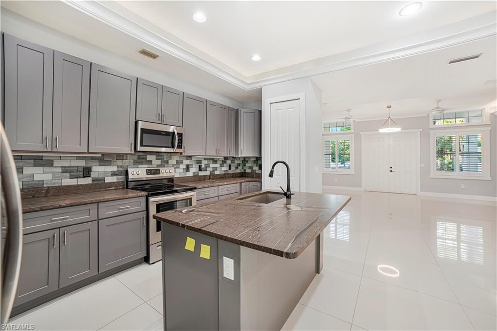 Kitchen featuring backsplash, a center island with sink, sink, gray cabinets, and appliances with stainless steel finishes