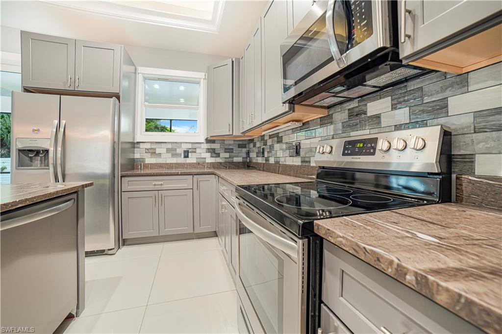Kitchen featuring decorative backsplash, gray cabinetry, stainless steel appliances, light tile patterned flooring, and light stone counters