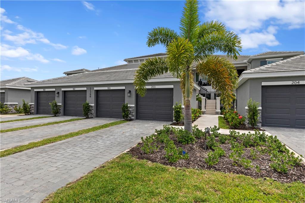 Contemporary residence featuring individual garage doors, stone veneer accents, and lush landscaping.