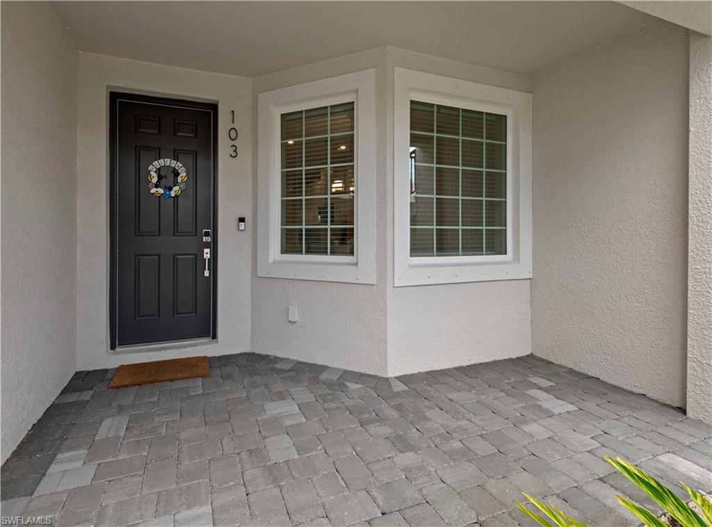 Entryway featuring textured stucco siding, a paneled front door with modern hardware, and a bay window with grid-patterned panes
