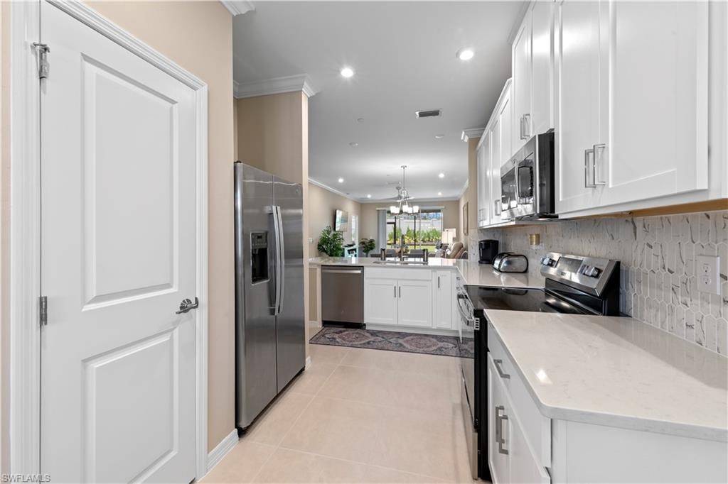 Modern kitchen featuring white cabinetry, stainless steel appliances, light-toned countertops, and a patterned tile backsplash
