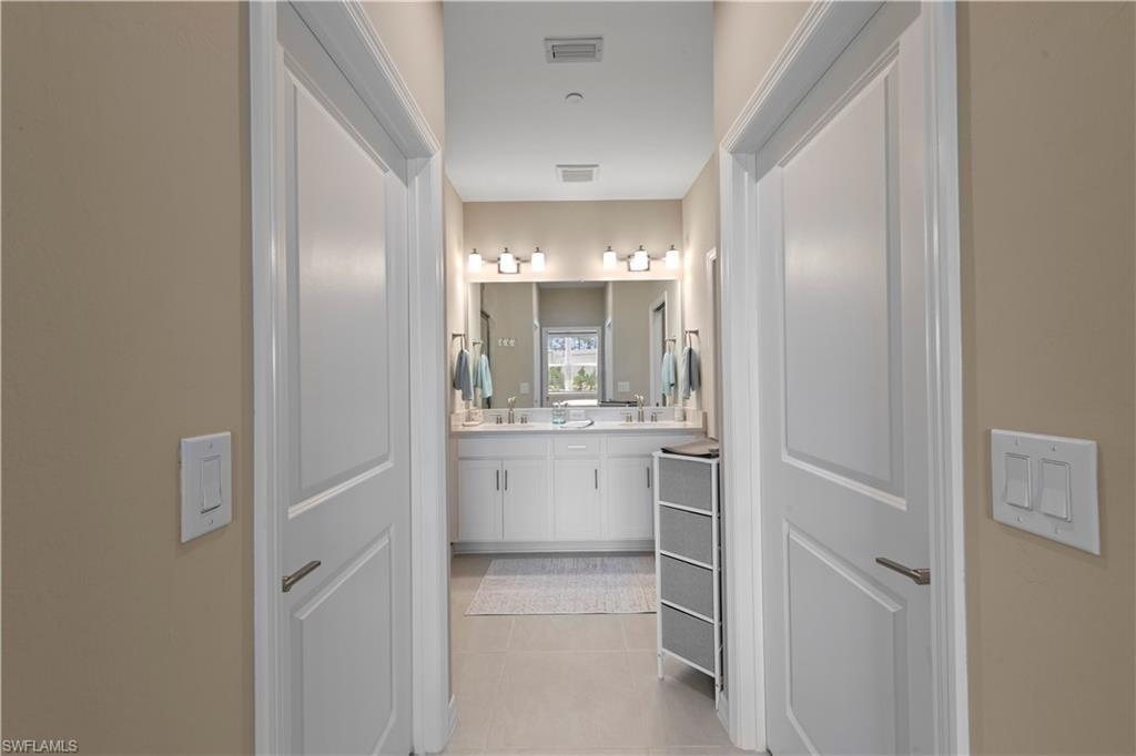 Lead from the Primary bedroom into the contemporary bathroom featuring a dual vanity with white cabinetry, a large mirror, and modern light fixtures
