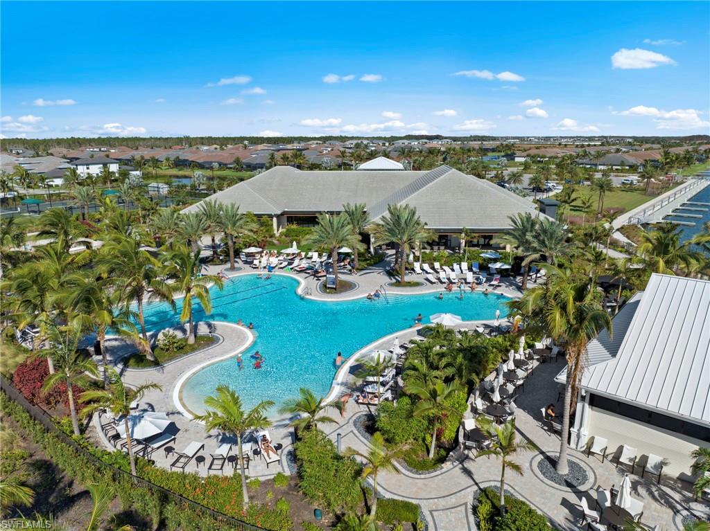 Expansive resort-style swimming pool surrounded by tropical landscaping, a central clubhouse, and TONS OF additional amenities