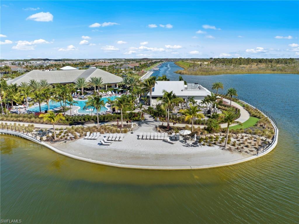 Expansive resort-style pool area with multiple buildings, surrounding water features, sandy beach, and established palm trees