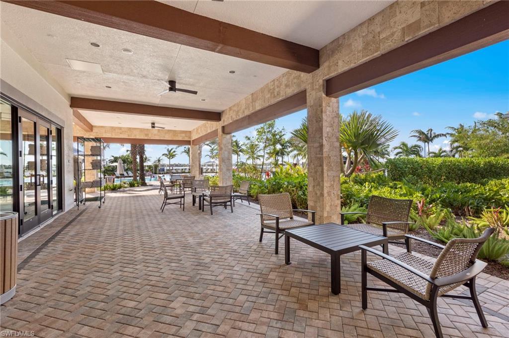 Expansive covered patio featuring herringbone paver flooring, robust stone pillars, and wood-finish ceiling beams
