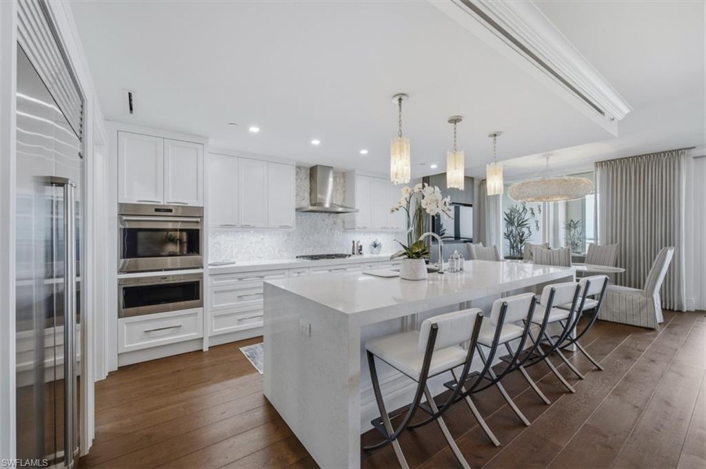 Gourmet kitchen featuring a waterfall island with seating, integrated stainless steel appliances, white shaker cabinetry, and a full-height tile backsplash