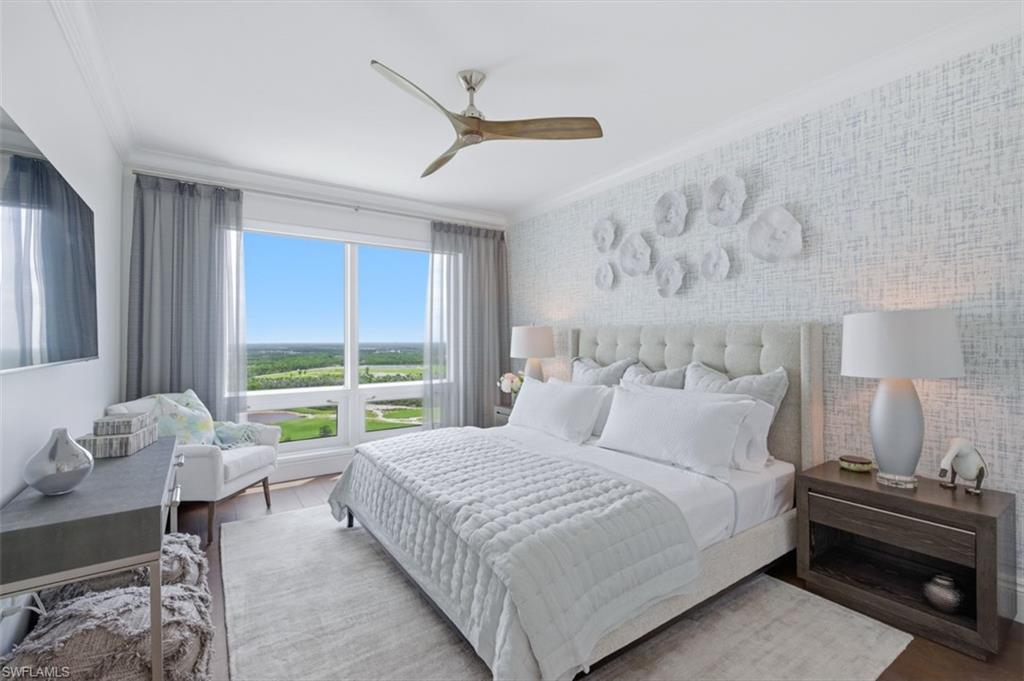 Expansive window offering a broad landscape, wood-finish flooring, tufted headboard, crown molding, and a modern ceiling fan