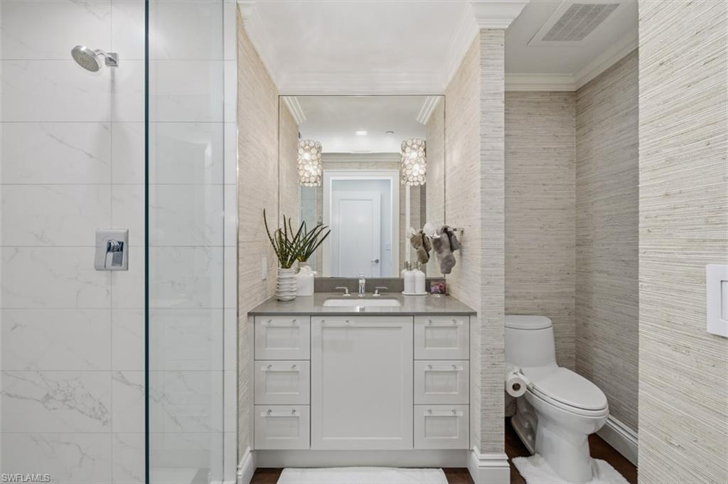 Bathroom featuring a glass-enclosed shower with white tiled walls, a single vanity with a light gray countertop and white cabinetry, a built-in toilet, and textured wall coverings throughout