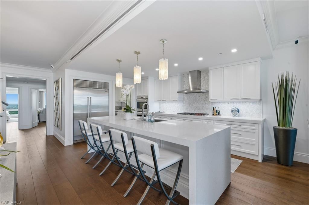 Gourmet kitchen with a waterfall island, stainless steel appliances, custom white cabinetry, quartz countertops, and mosaic tile backsplash
