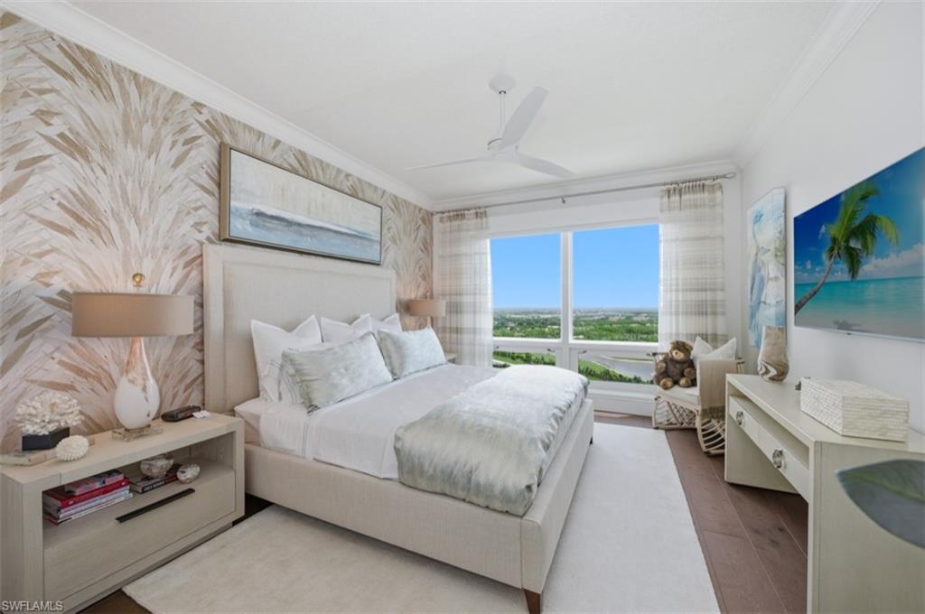 Spacious sleeping area featuring a patterned accent wall, crown molding, a ceiling fan, large windows, and dark wood-finish flooring