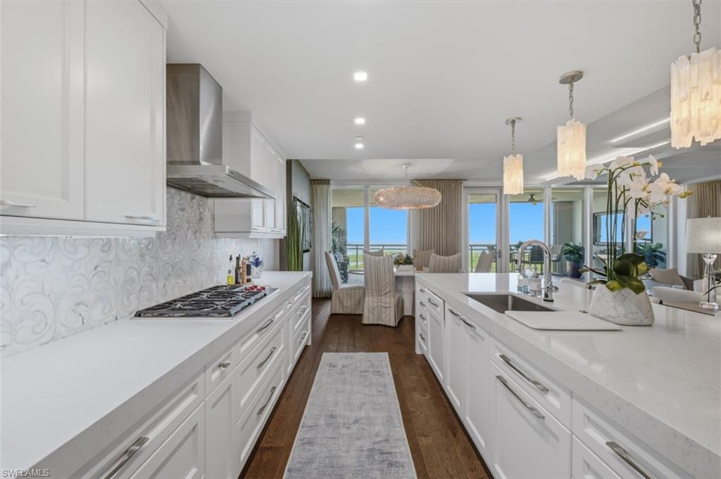 Gourmet kitchen featuring white shaker cabinetry, an integrated gas cooktop, decorative backsplash, a stainless steel range hood, and wood-finish flooring
