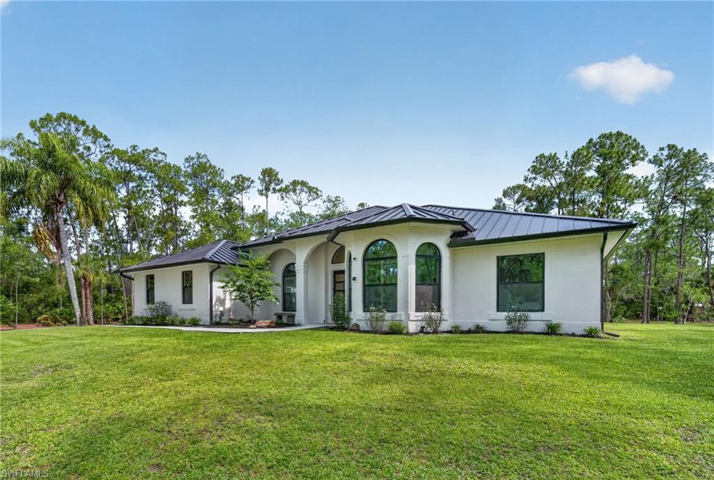 White brick exterior featuring a dark metal roof, arched windows, and a manicured lawn