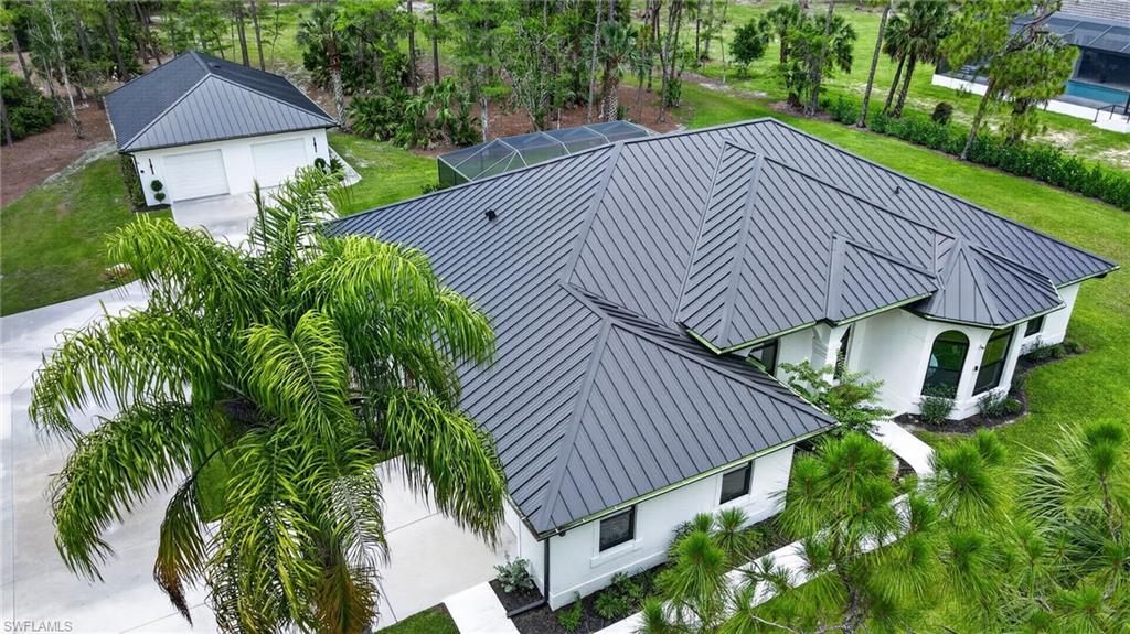 Contemporary residence featuring a dark metal roof, white stucco exterior, multiple arched windows, and lush green landscaping