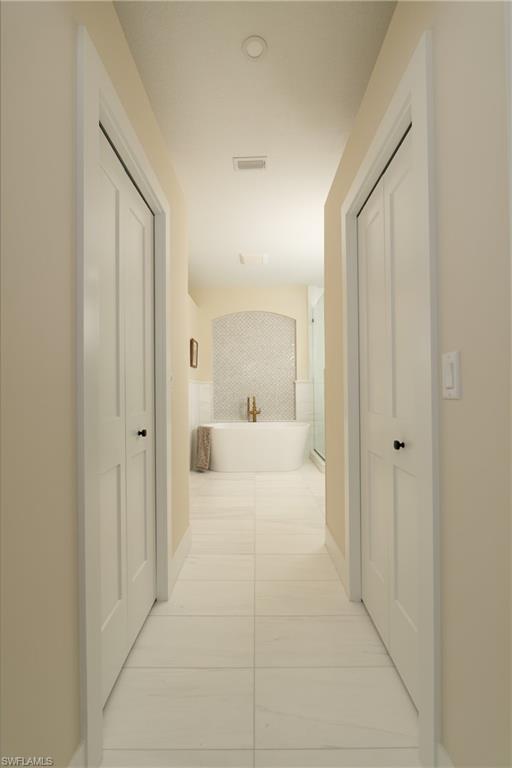 Hallway featuring recessed lighting, paneled doors, and large format tile flooring, leading to a freestanding soaking tub with a tiled accent wall