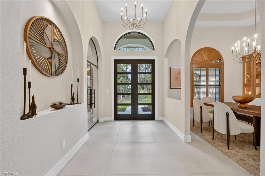 Grand entry foyer featuring light-toned flooring, arched doorways, a coffered ceiling, a contemporary chandelier, and double entry doors with transom window