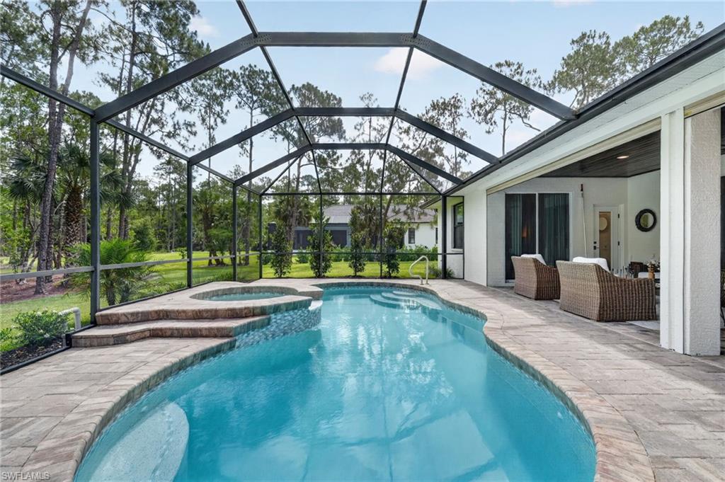 Screened outdoor living area featuring a freeform swimming pool with integrated spa and paver decking