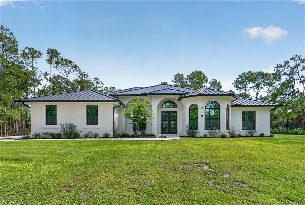 Contemporary exterior featuring a white brick facade, dark metal roof, arched entry, arched windows, and a manicured lawn