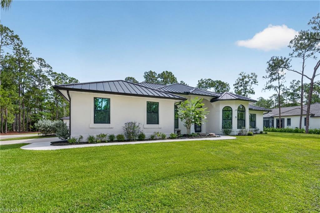Contemporary stucco exterior featuring a dark metal roof, arched windows, and a paved driveway