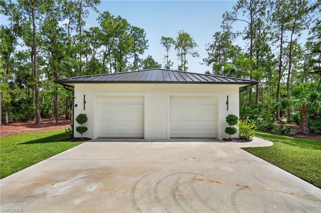 Two-car garage with white paneled doors, a dark metal roof, white stucco exterior, and black vertical sconces