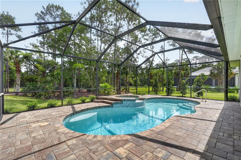 Screened enclosure featuring a freeform swimming pool with integrated spa, paver patio, and lush perimeter landscaping