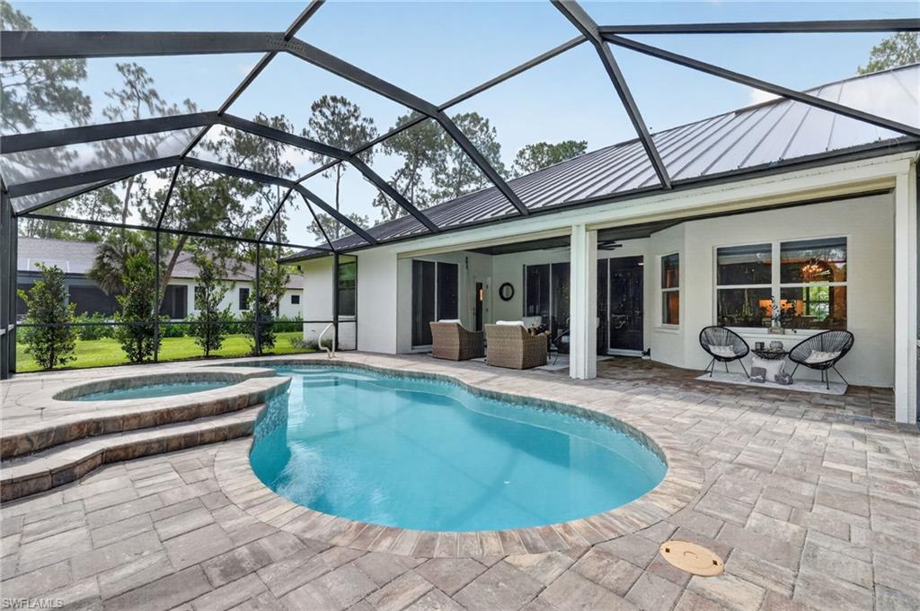 Screened outdoor living area featuring a freeform pool, integrated spa, and paver decking