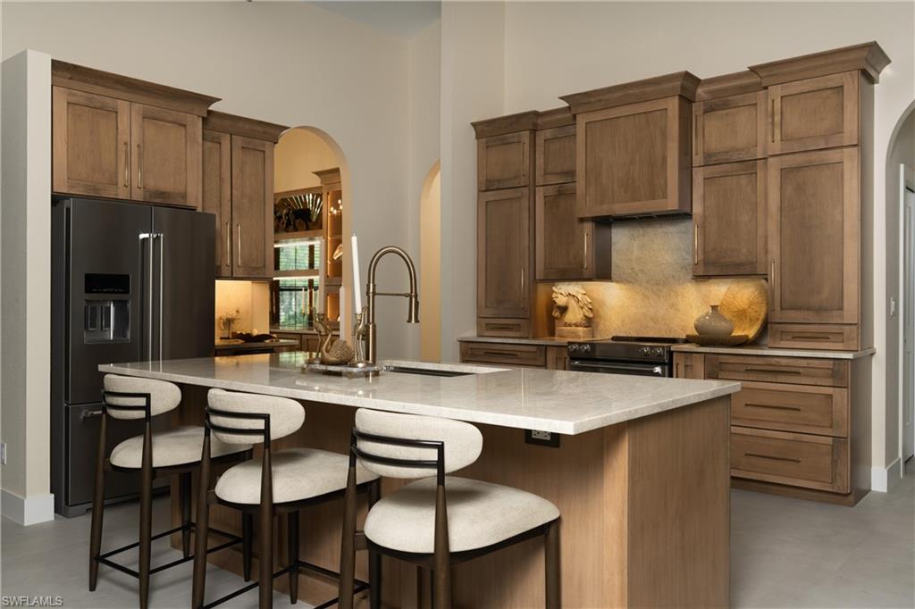 Gourmet kitchen featuring a central island with countertop seating, wood-finish cabinetry, stainless steel appliances, and elegant arched doorways