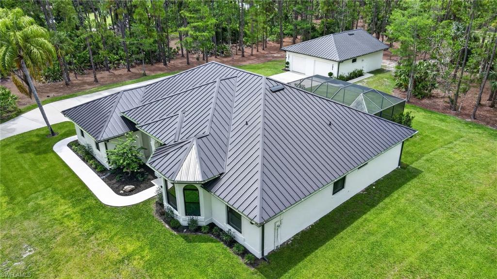 Expansive property featuring a main residence with a dark metal standing seam roof, a detached auxiliary building, and a screened enclosure