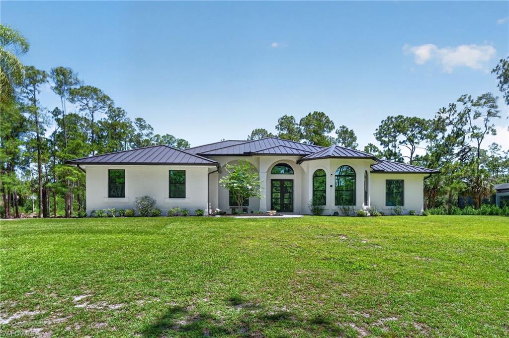 Contemporary-style exterior featuring a white stucco finish, dark metal roof, arched entryways, dark-framed windows, and a manicured lawn