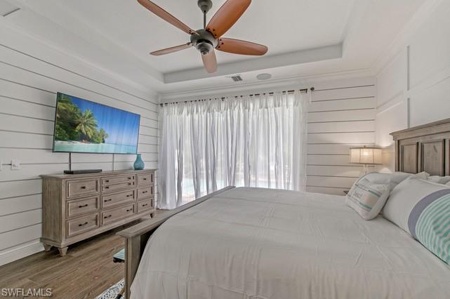 Recessed tray ceiling with a ceiling fan, shiplap wall finishes, and wood-finish flooring