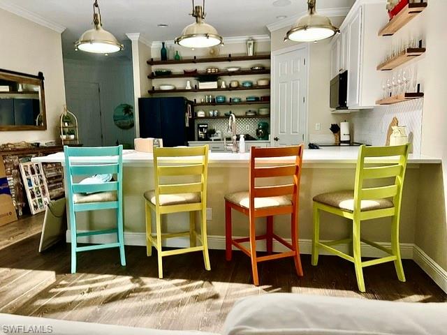 Kitchen island with light-toned countertop, pendant lighting, open shelving, white cabinetry, and wood-finish flooring