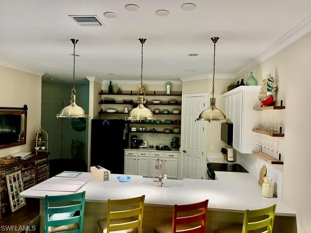 Open-concept kitchen featuring an expansive island with white countertop, three brass pendant lights, white cabinetry, and recessed ceiling lights