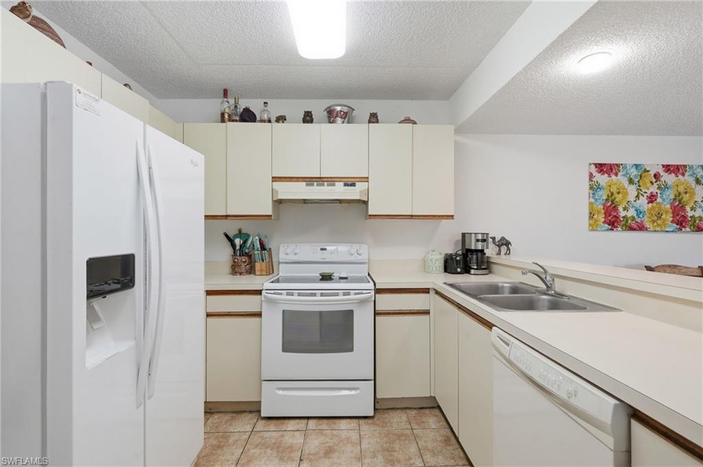 Kitchen featuring white appliances, cream cabinetry, light-toned countertops, and tile flooring