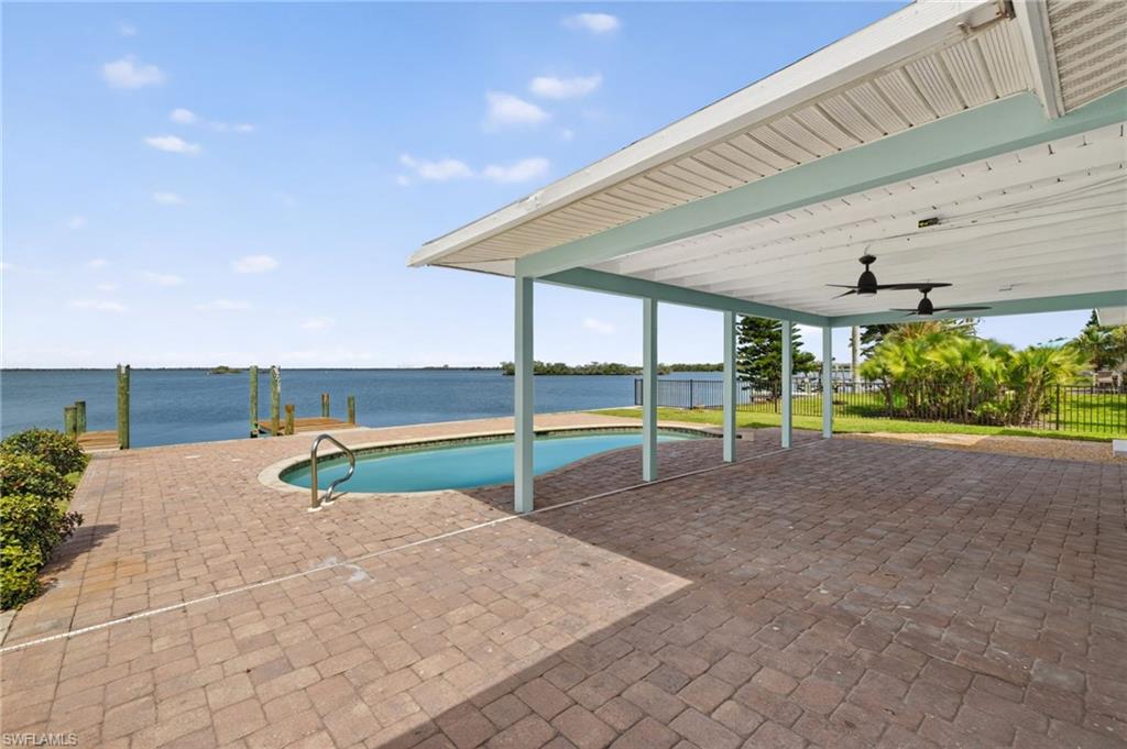 Covered patio featuring an inground pool, brick paver flooring, waterfront access with a wooden dock, and ceiling fans