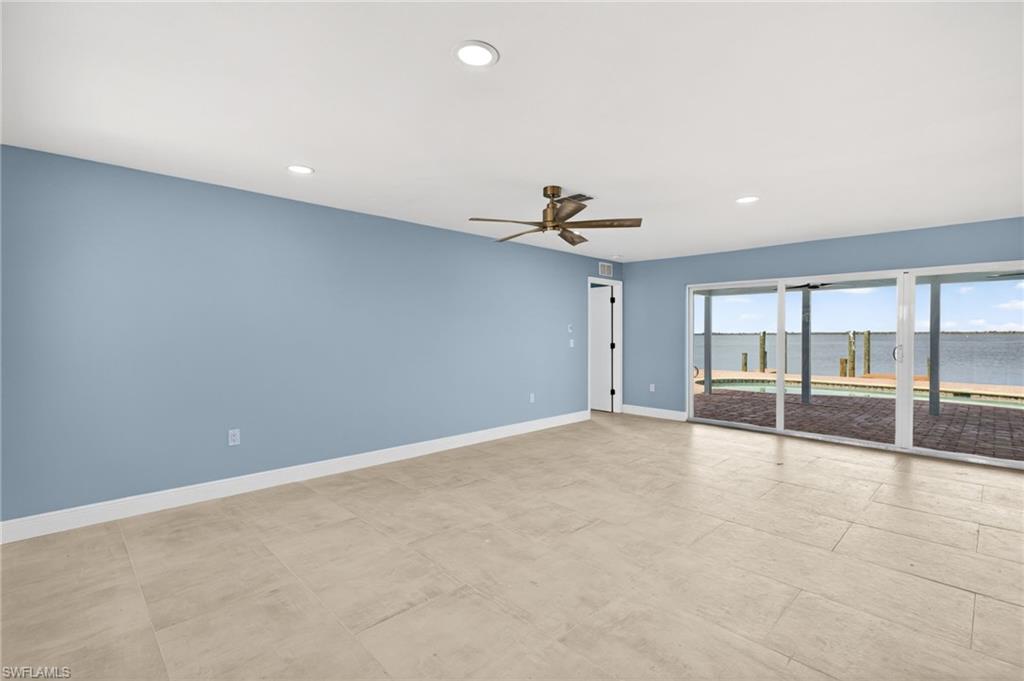 Spacious interior featuring light-toned tile flooring, recessed ceiling lighting, a contemporary ceiling fan, and expansive sliding glass doors opening to a waterfront patio with a dock