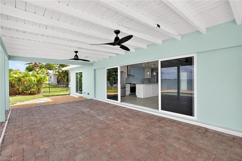 Spacious covered patio with brick paver flooring, exposed white wood beam ceiling, and two ceiling fans