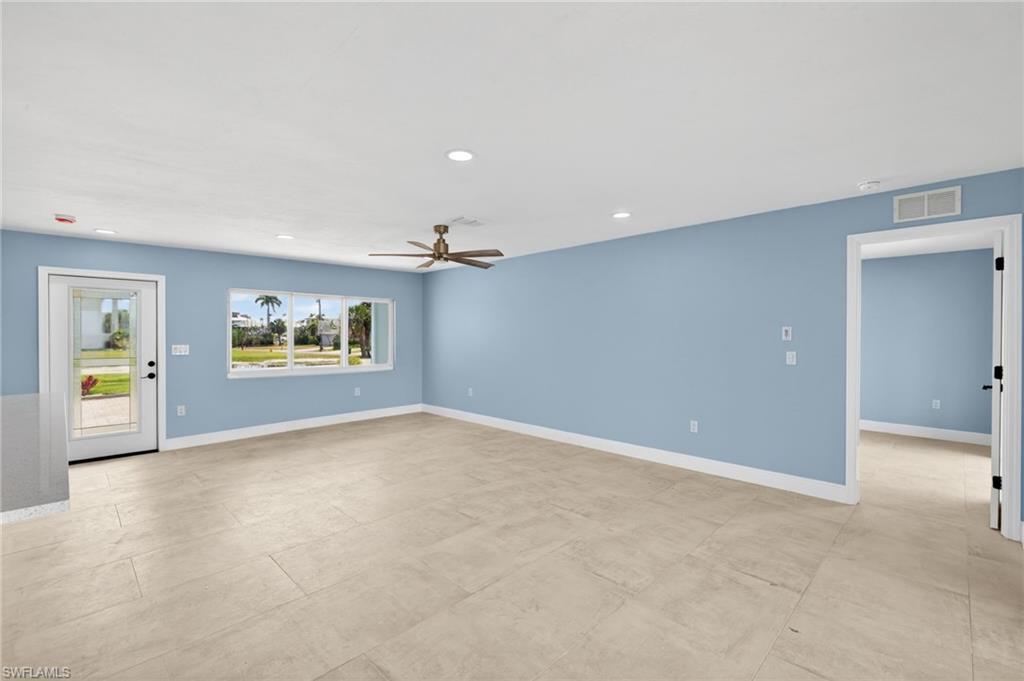 Spacious interior with neutral tile flooring, recessed lighting, a modern ceiling fan, and a large window overlooking exterior landscaping
