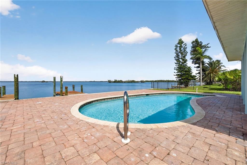 Curved swimming pool with a stainless steel handrail, surrounded by paver patio decking