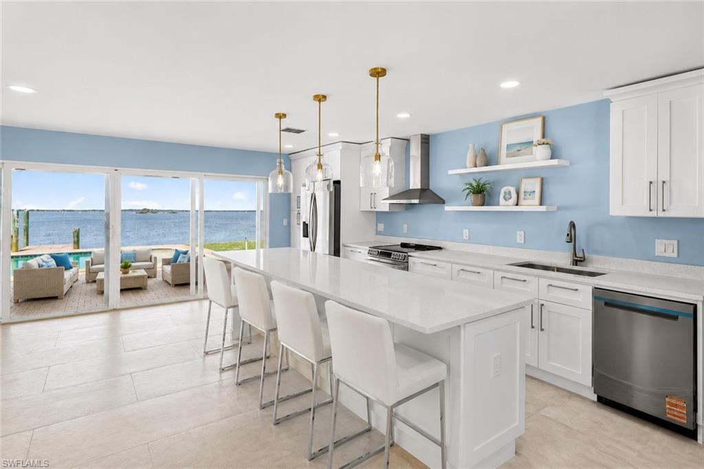 Open-concept kitchen with white cabinetry and a large center island, featuring stainless steel appliances and stone countertops
